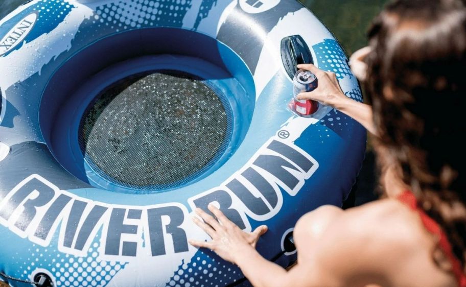 a woman putting a soft drink can in a cup holder on an tube pool float