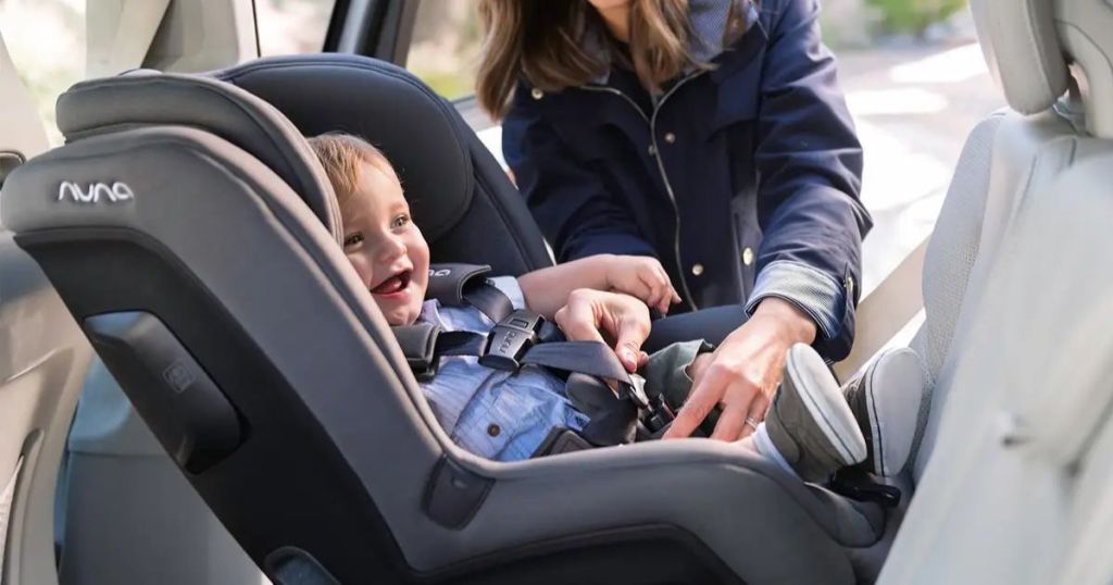 Nuna RAVA™ Flame Retardant Free Convertible Car Seat shown with baby inside and mom buckling baby in 