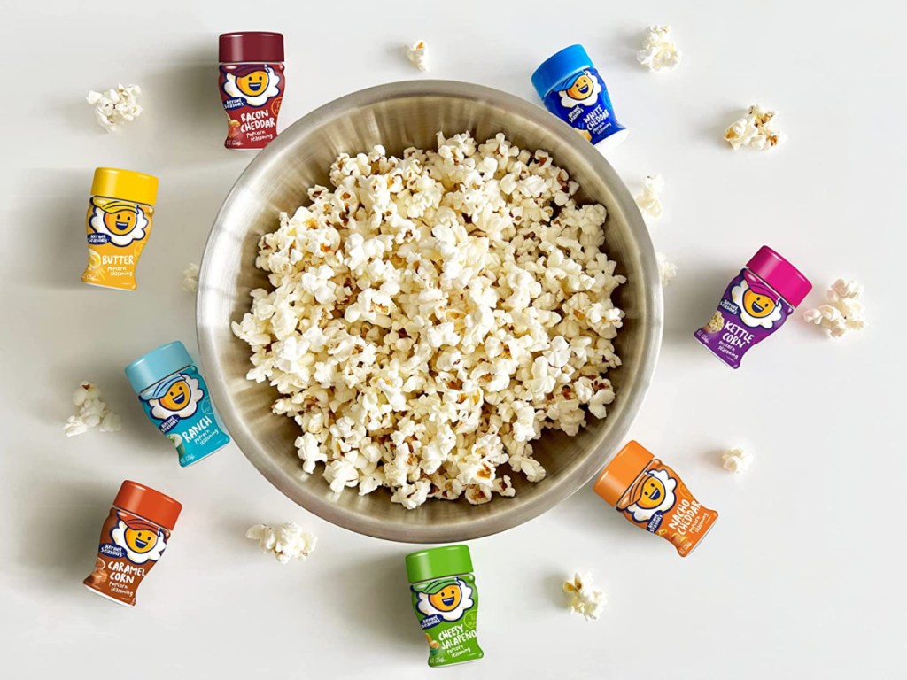 A bowl of popcorn surrounded by 8 mini jars of Kernel Season's Popcorn Seasoning
