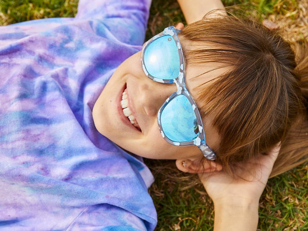 girl laying in grass wearing cloud print sunglasses