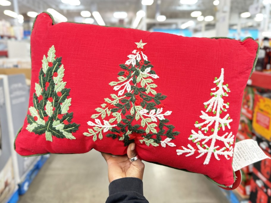 hand holding up a red throw pillow with embroidered trees