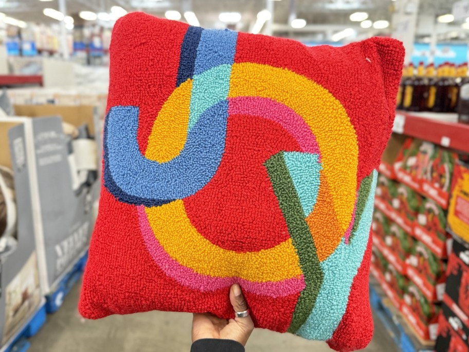 hand holding a colorful throw pillow that says joy