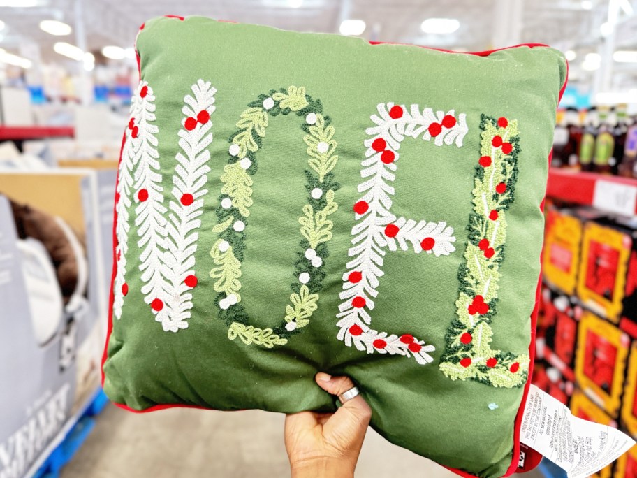 hand holding up a green throw pillow that says noel