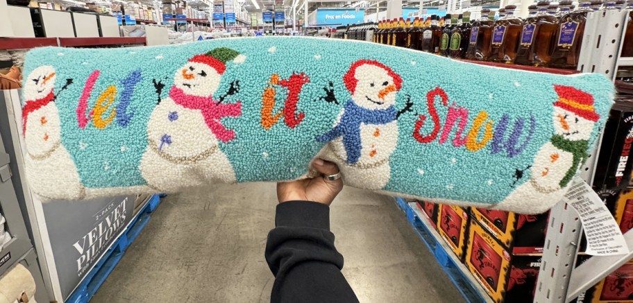 hand holding a long throw pillow that says "let it snow" with snowmen print