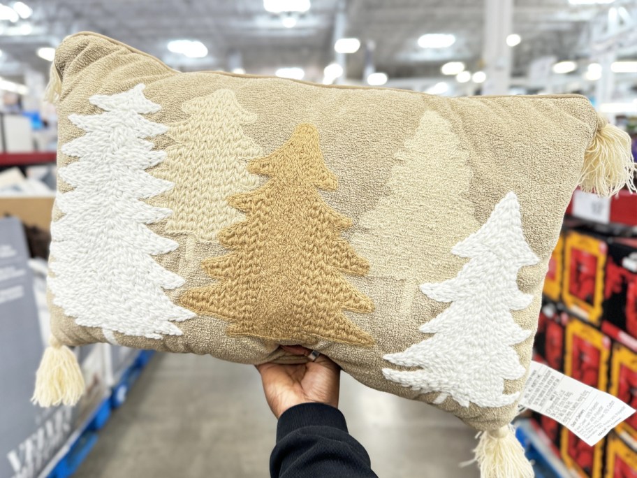 hand holding a tan throw pillow with textured trees