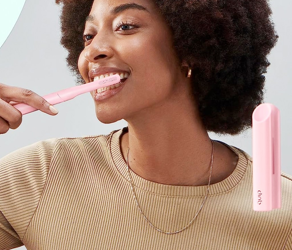 woman looking in mirror while brushing her teeth with a pink toothbrush