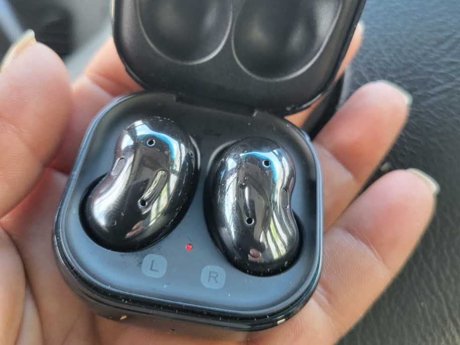 hand holding an opened black case with samsung buds inside