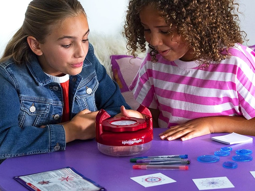 two girls playing with spirograph set