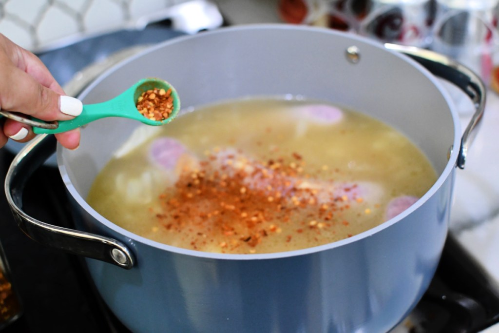 adding red pepper flakes to beer brats in a pot