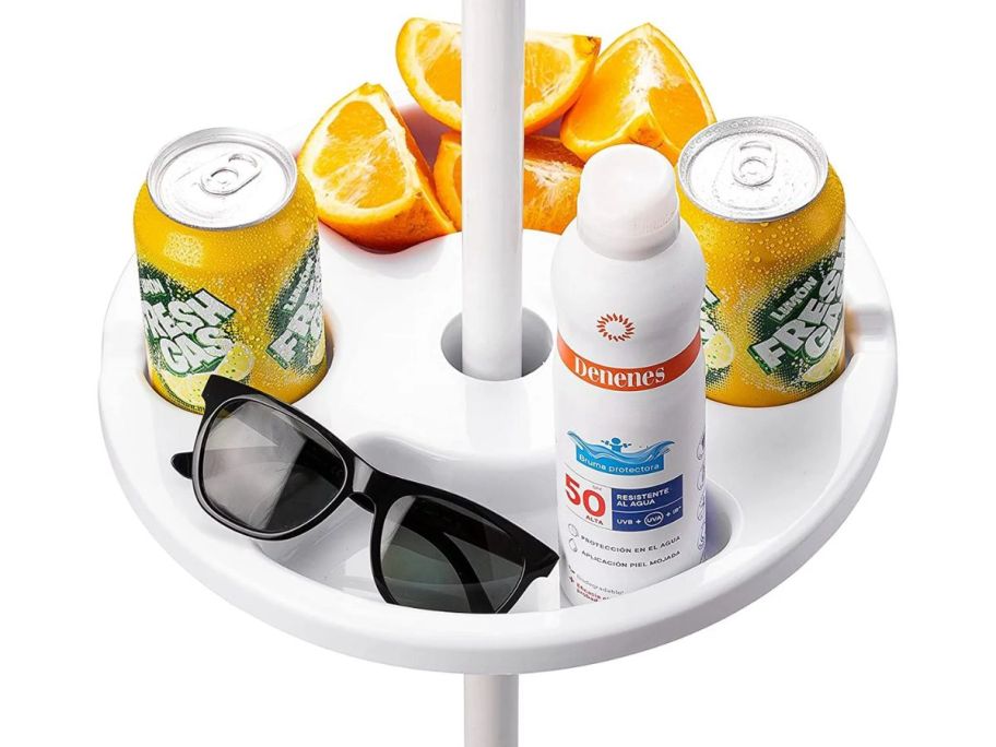 a white beach umbrella tray table with sunglasses, sun screen, and sliced oranges in the large onlinepartments and two cans of soda in the cup holders. on a white back ground