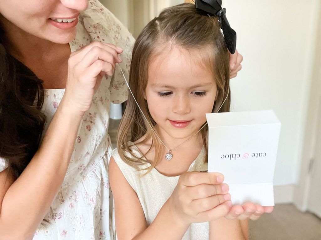 woman putting heart necklace around little girls neck