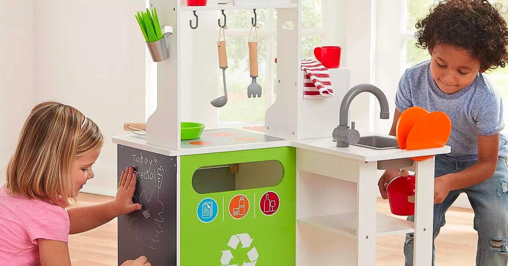 two kids playing with gray and green wooden play kitchen