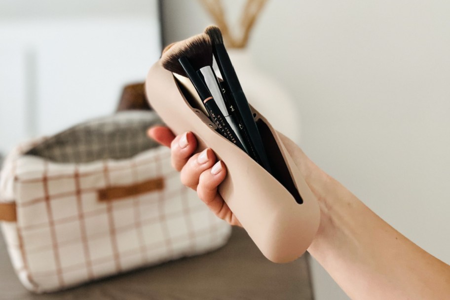 hand holding tan makeup brush case with brushes in them