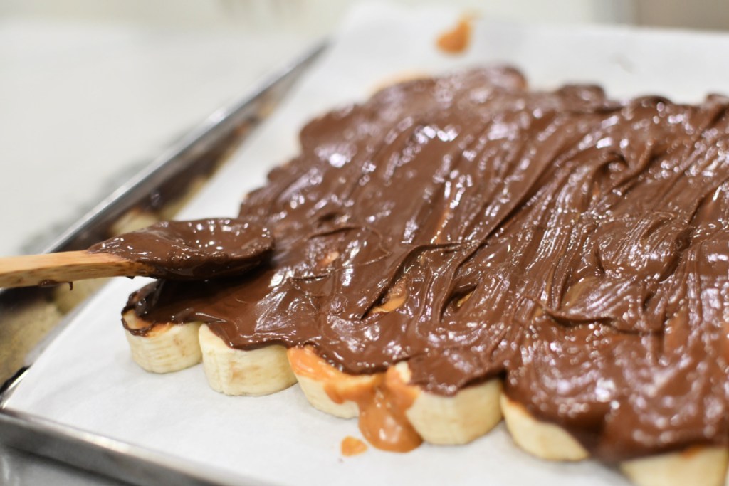 spreading chocolate on top of peanut butter and bananas