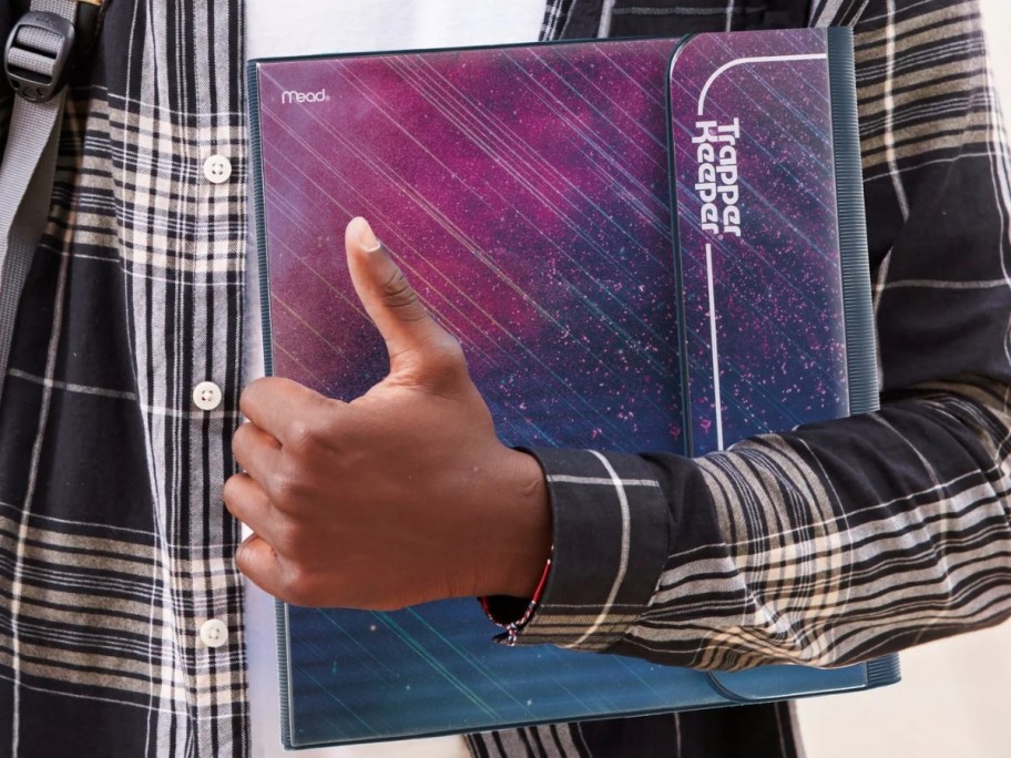 person in black plaid flannel shirt holding a Trapper Keeper with purple, blue, teal meteor shower design