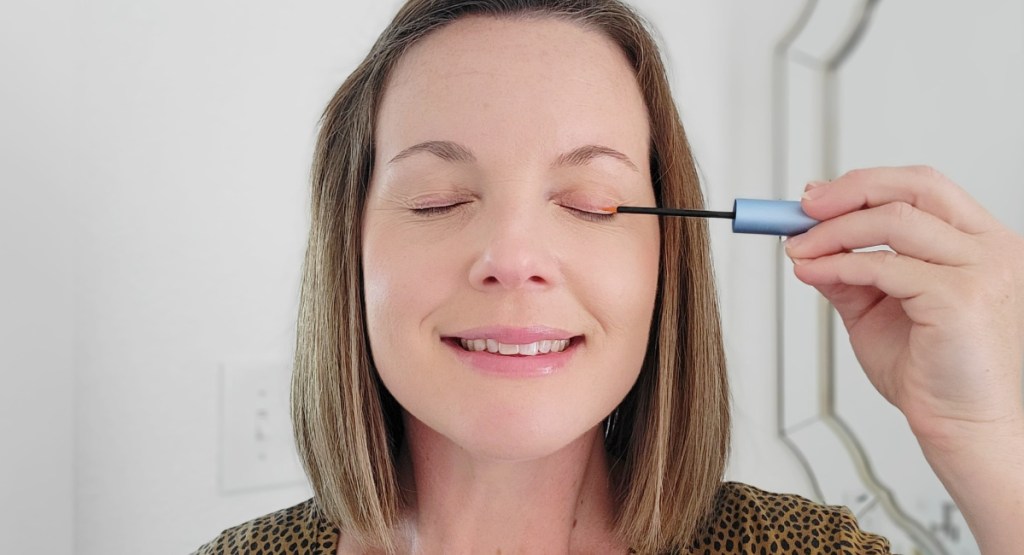 woman using lash growth serum wand on her lids