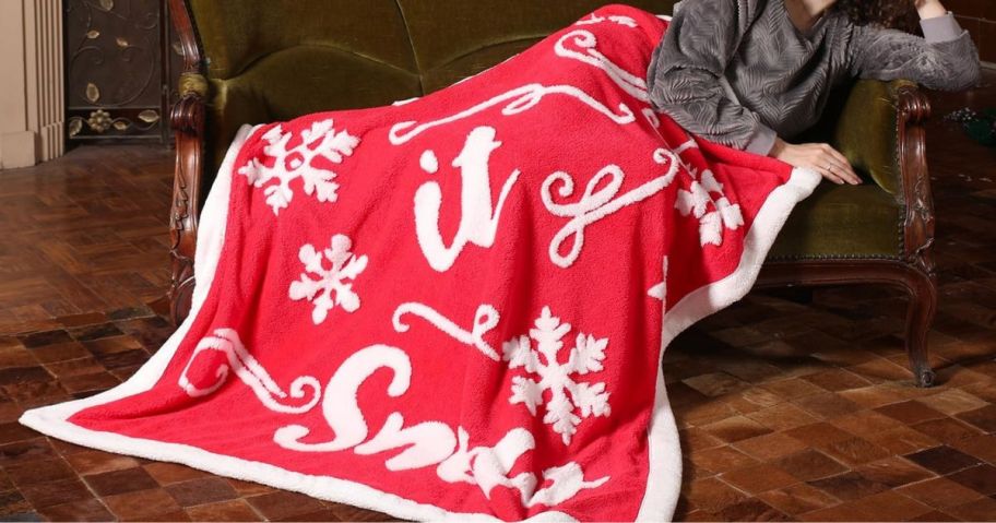 A woman on a couch with a red "Let It Snow" blanket