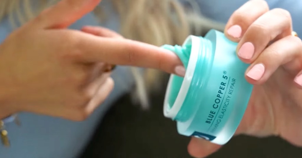 woman scooping out blue colored cream from lotion container