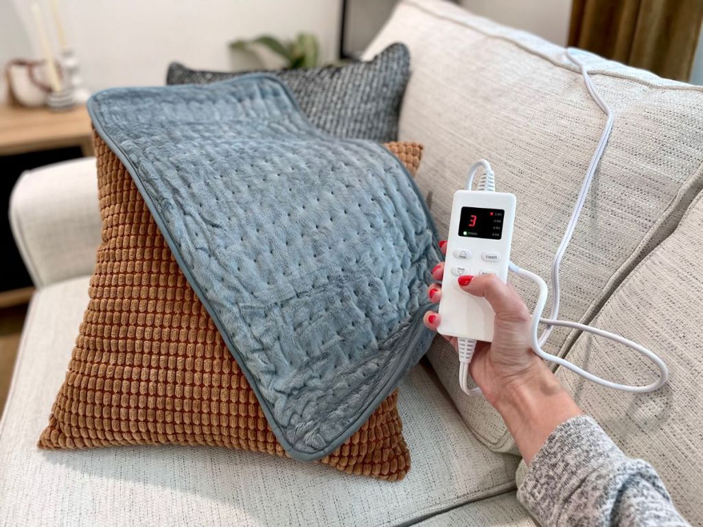 person holding remote to blue heating pad which is laying acroos brown pillow