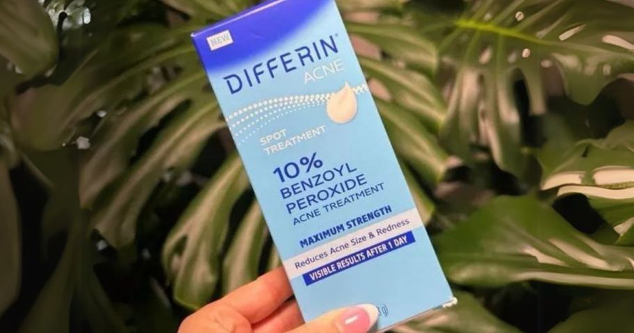 hand holding Differin Acne Spot Treatment Gel 1oz Tube in front of plant