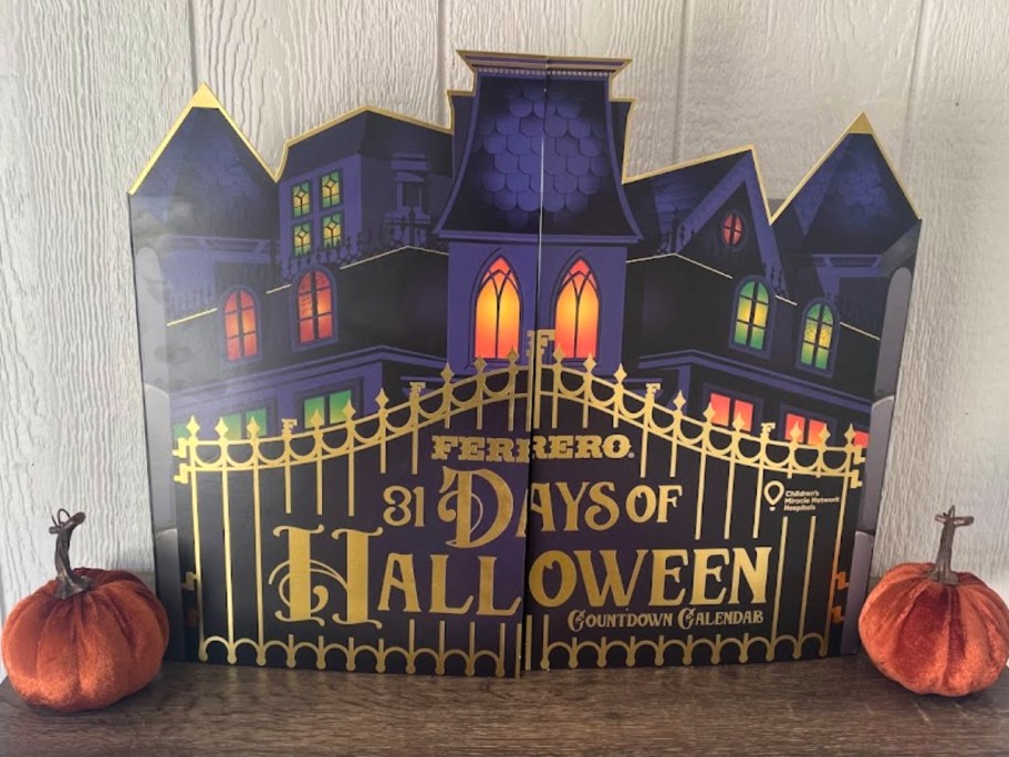 Ferrero Halloween Countdown Calendar in a purple, black and gold haunted mansion shaped box on a table with small pumpkins