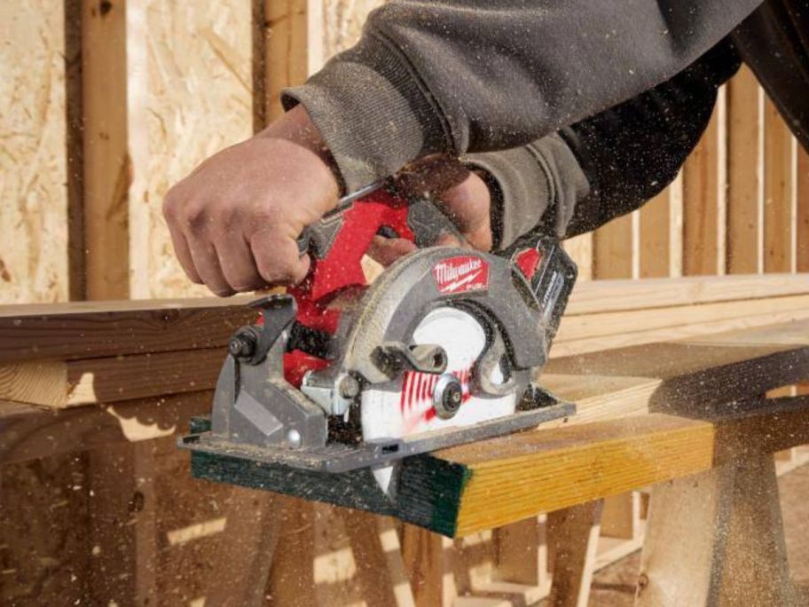 A man's hands using a Milwaukee M18 FUEL 18V Lithium-Ion Brushless Cordless Circular Saw  to cut wood