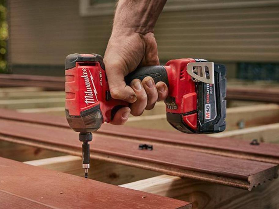 Hand using a Milwaukee M18 Fuel Surge 18V Lithium-Ion Brushless Cordless Hex Impact Driver to screw a nail into a wood plank