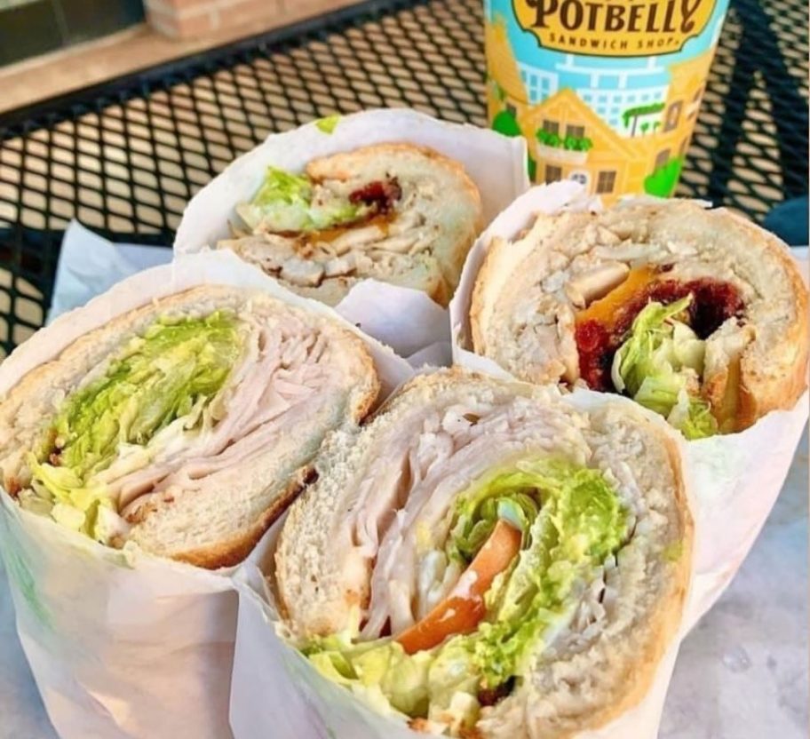 Two Potbelly Sandwiches cut open with the insides exposed next to a fountain drink cup