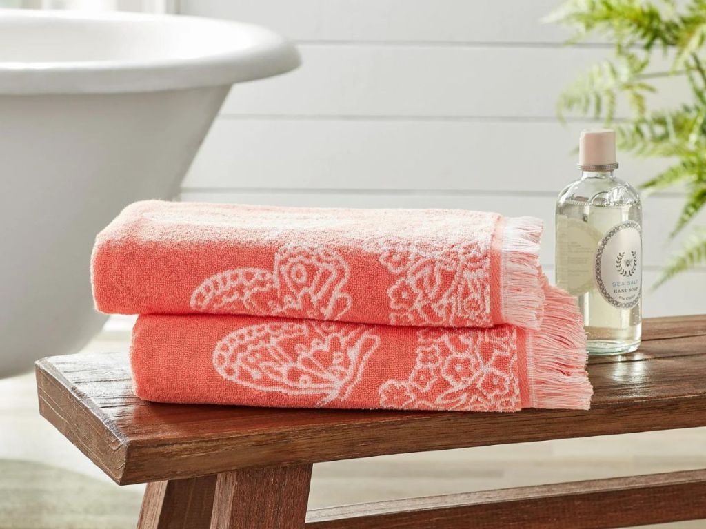 A bench next to a bath tub with Pioneer Woman bath towels on it 