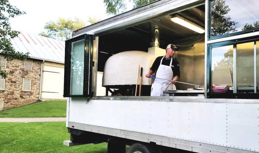 person making pizza in open air food truck