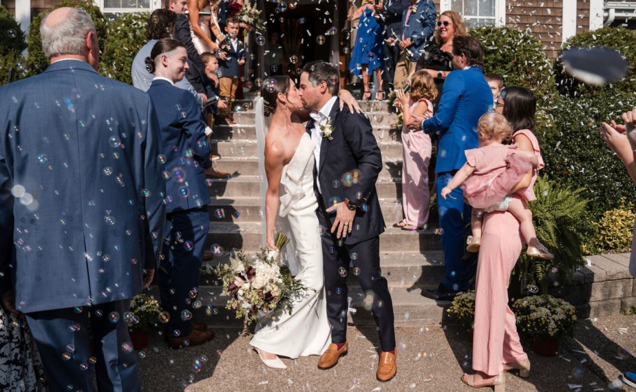 bride and groom kissing surrounded by wedding guests and bubbles