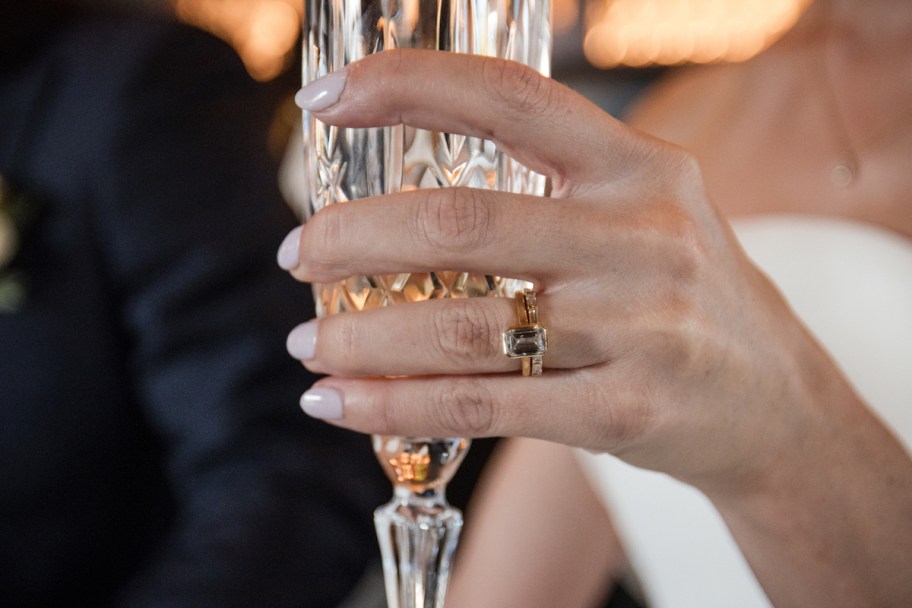 close up of brides wedding ring holding crystal champagne flute