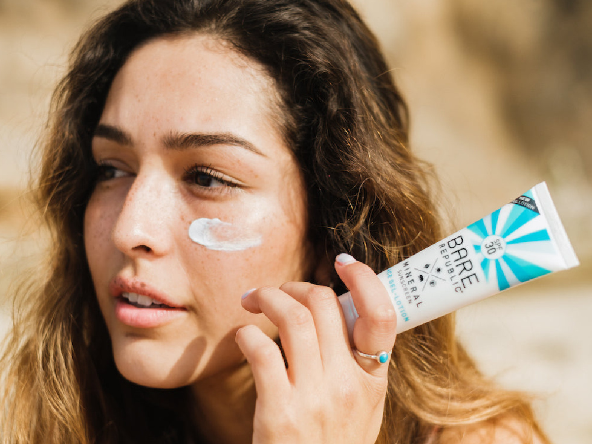 woman with sunscreen applied on her face and holding the bottle