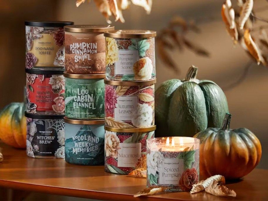 fall candles stacked on table with candle burning in front with pumpkins 