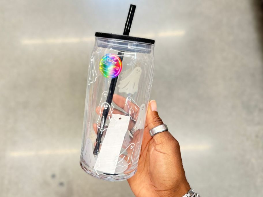 hand holding a glass tumbler with ghost designs on it and black lid and straw