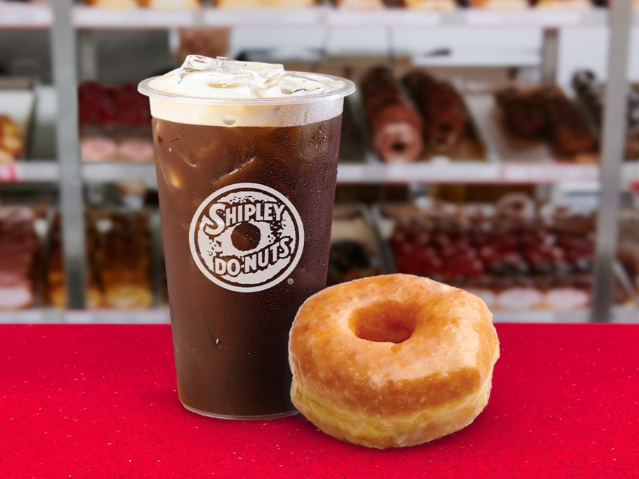 iced coffee next to a glazed donut on a red table