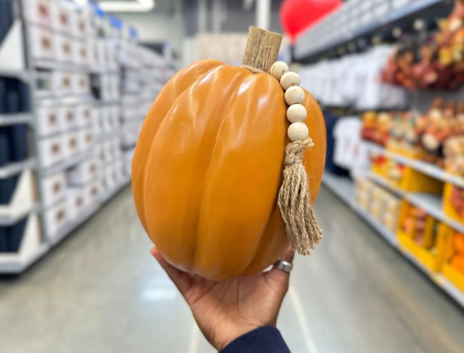 a woman's hand holding a ceramic pumpkin with beaded cord