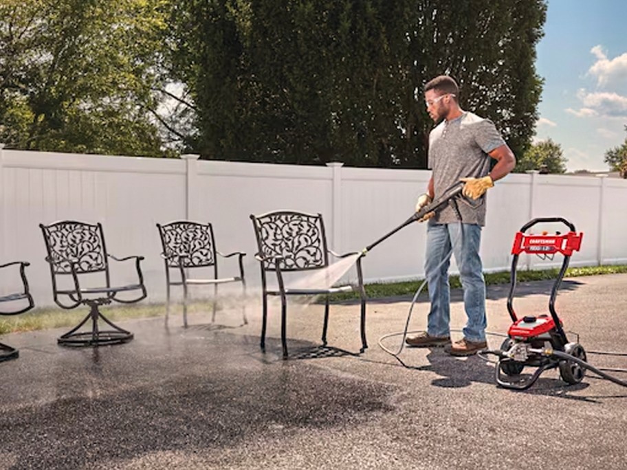 man using red and black pressure washer on chairs