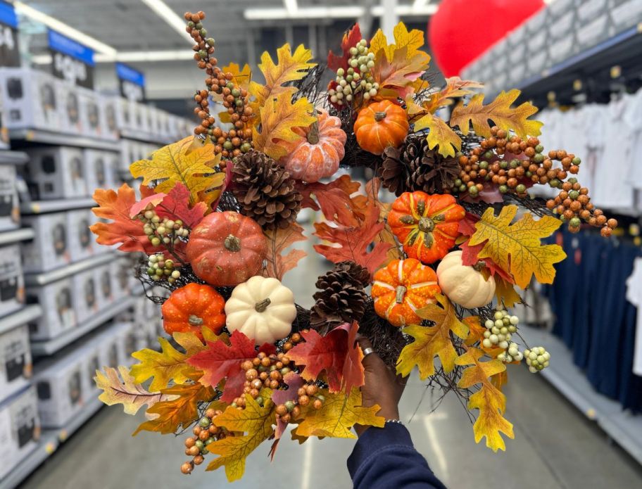 a woman's hand holding a lush fall themed wreath