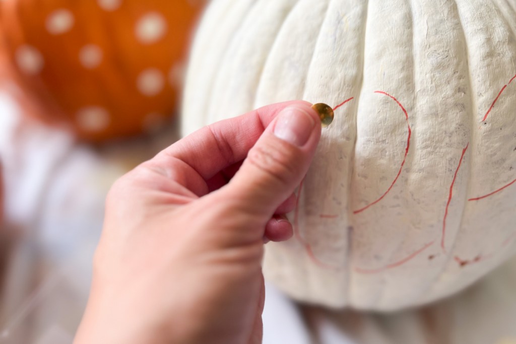 gold thumbtack going into white pumpkin