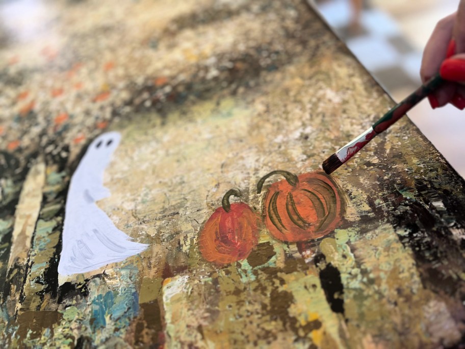 painting pumpkins on a thrift store canvas painting for halloween