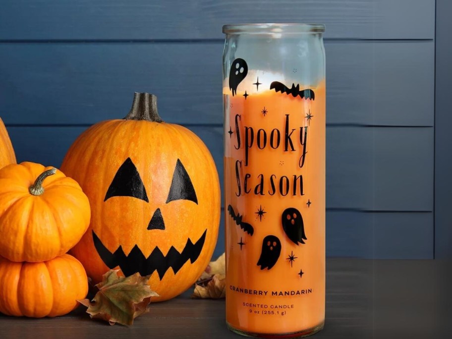 orange candle in a glass that says Spooky Season and have ghosts on it next to a jackolantern and pumpkins