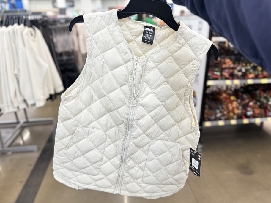 holding up a white quilted vest on hanger in store