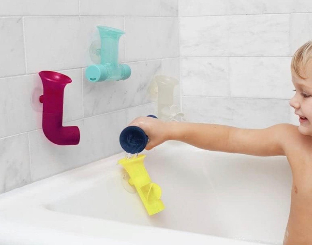 toddler in bathtub playing with suction cup toys on tile wall