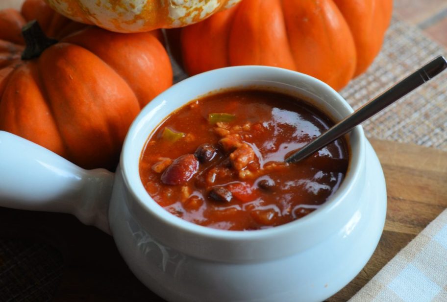 A bowl of pumpkin chili in front of pumpkins