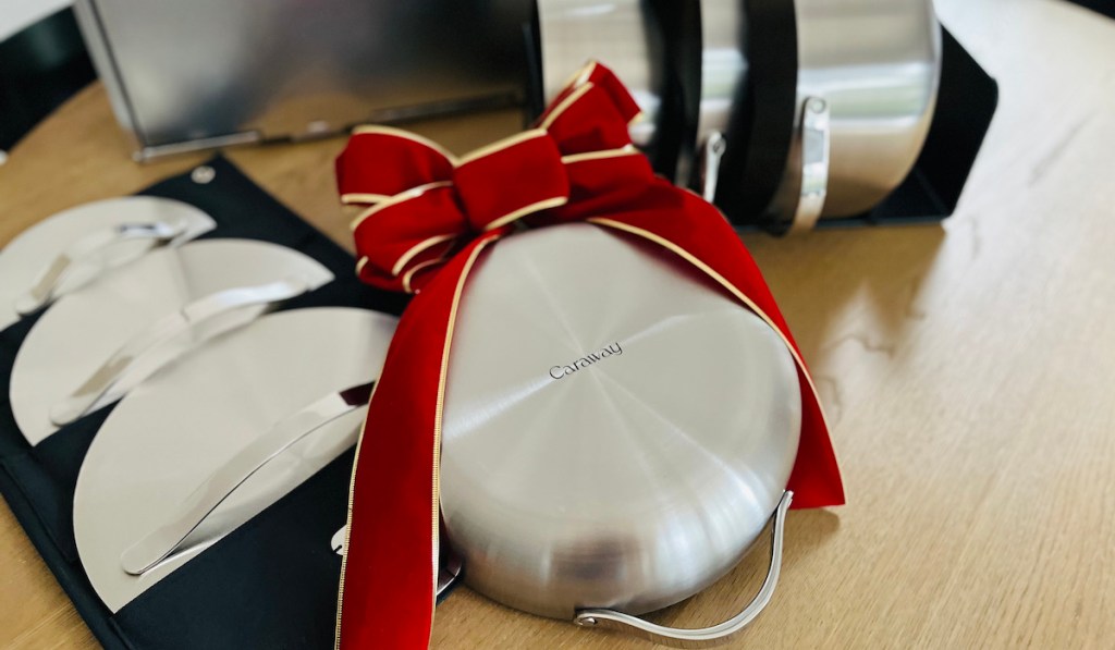 Bottom of stainless steel Caraway cooking pan with big red bow on wood table with set 