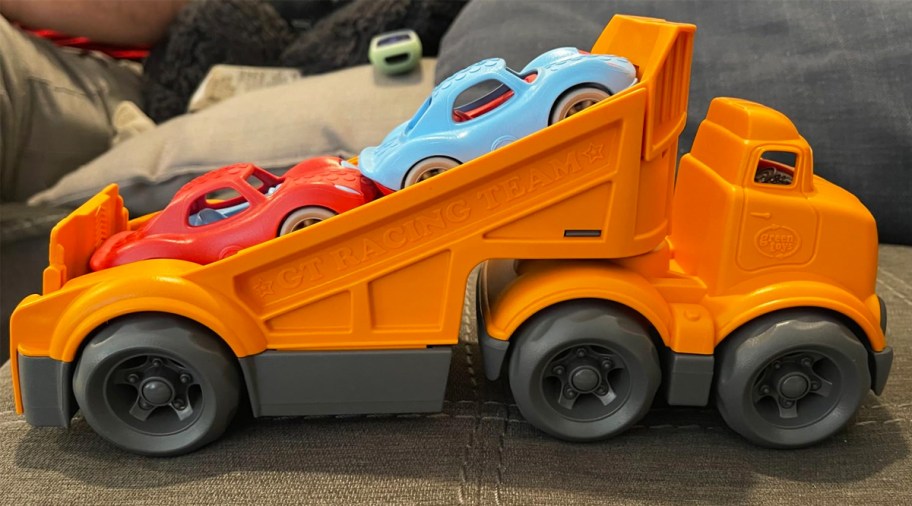 orange toy truck with red and blue race cars on truck bed