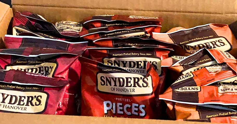 an open cardboard box with individual bags of Snyders Pretzels in different flavors