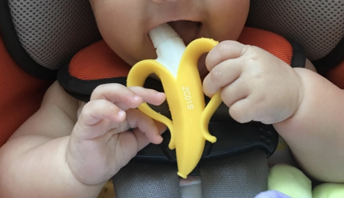 baby in car seat holding banana shaped teether in mouth 