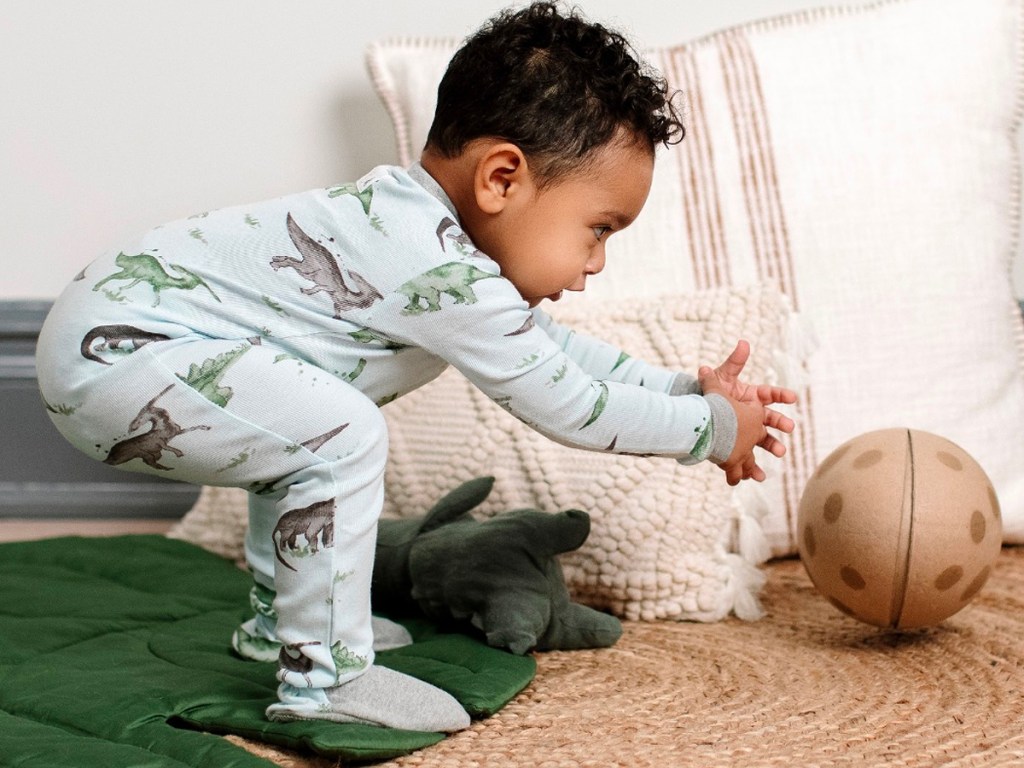 baby wearing blue dinosaur pajamas trying to get ball 